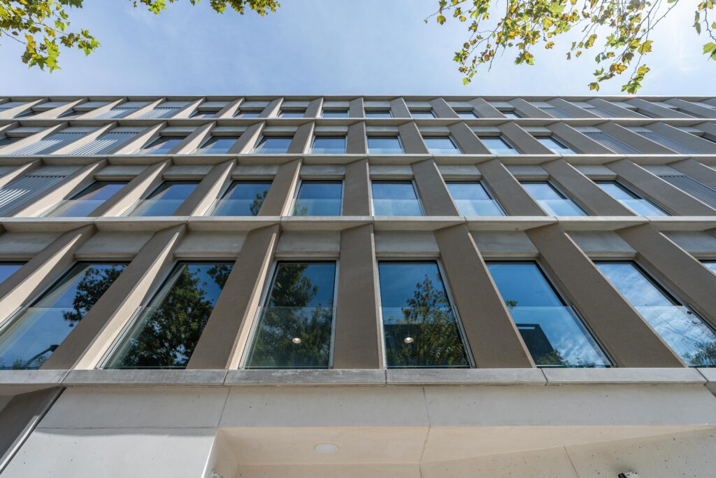 Vista contrapicada de la fachada de la residencia para mayores en Llacuna, Barcelona, con ventanas verticales, estructura modular y arbolado urbano.