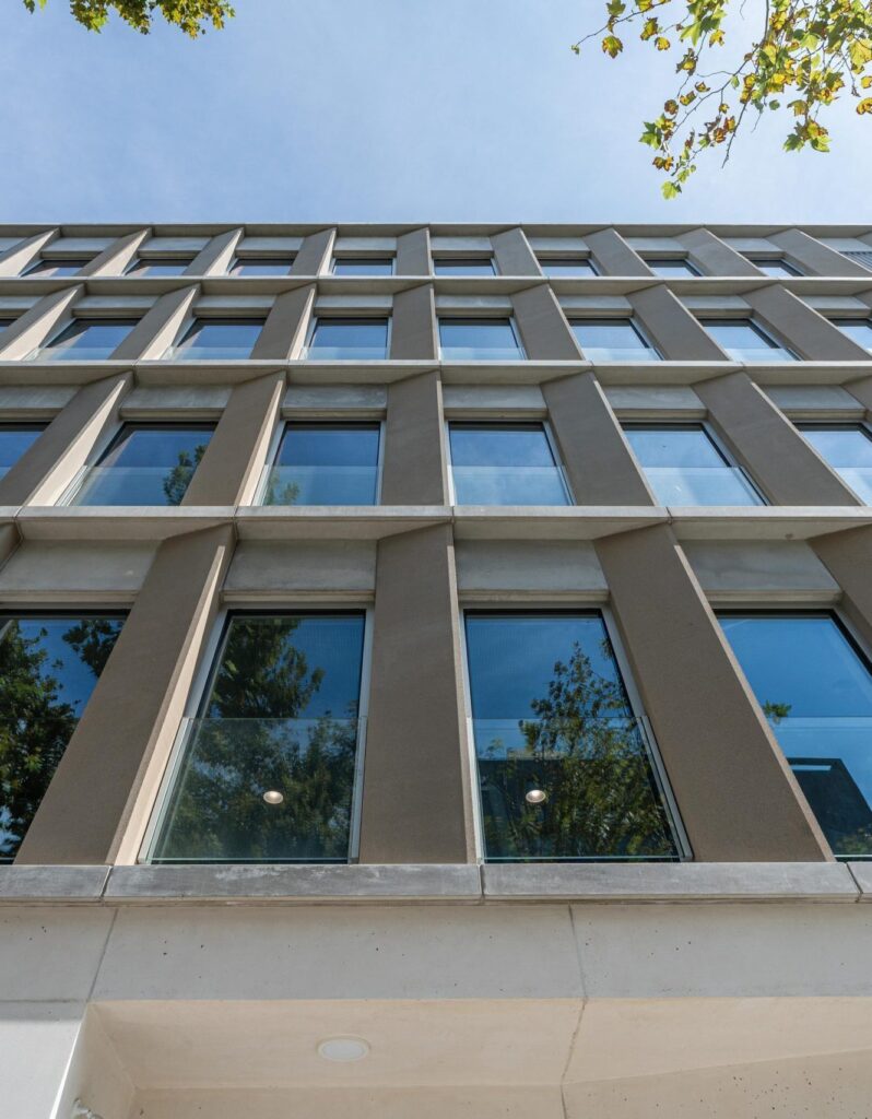 Vista contrapicada de la fachada de la residencia para mayores en Llacuna, Barcelona, con ventanas verticales, estructura modular y arbolado urbano.